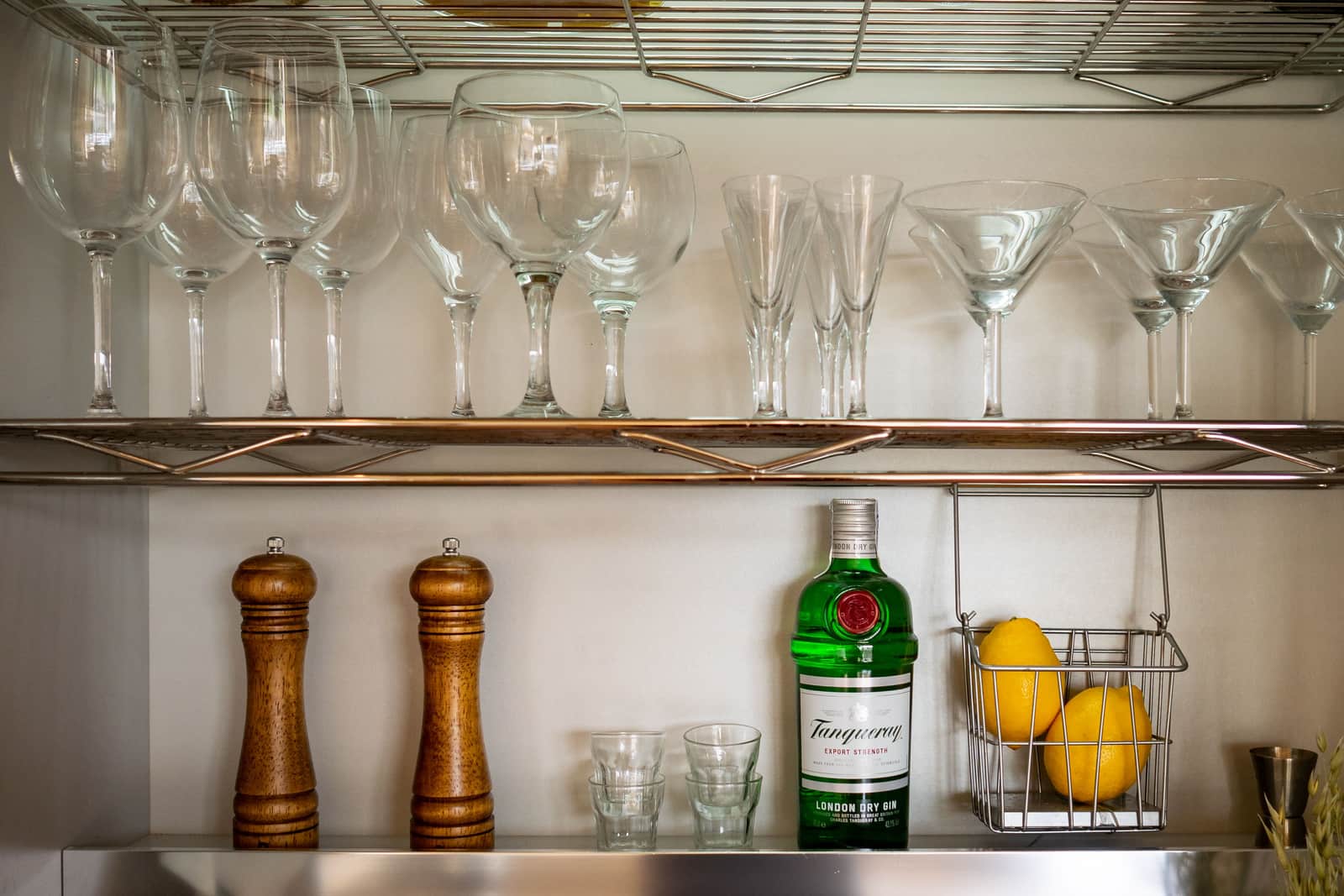 A two-tier bar cart holding bottles and glassware against a warm wall