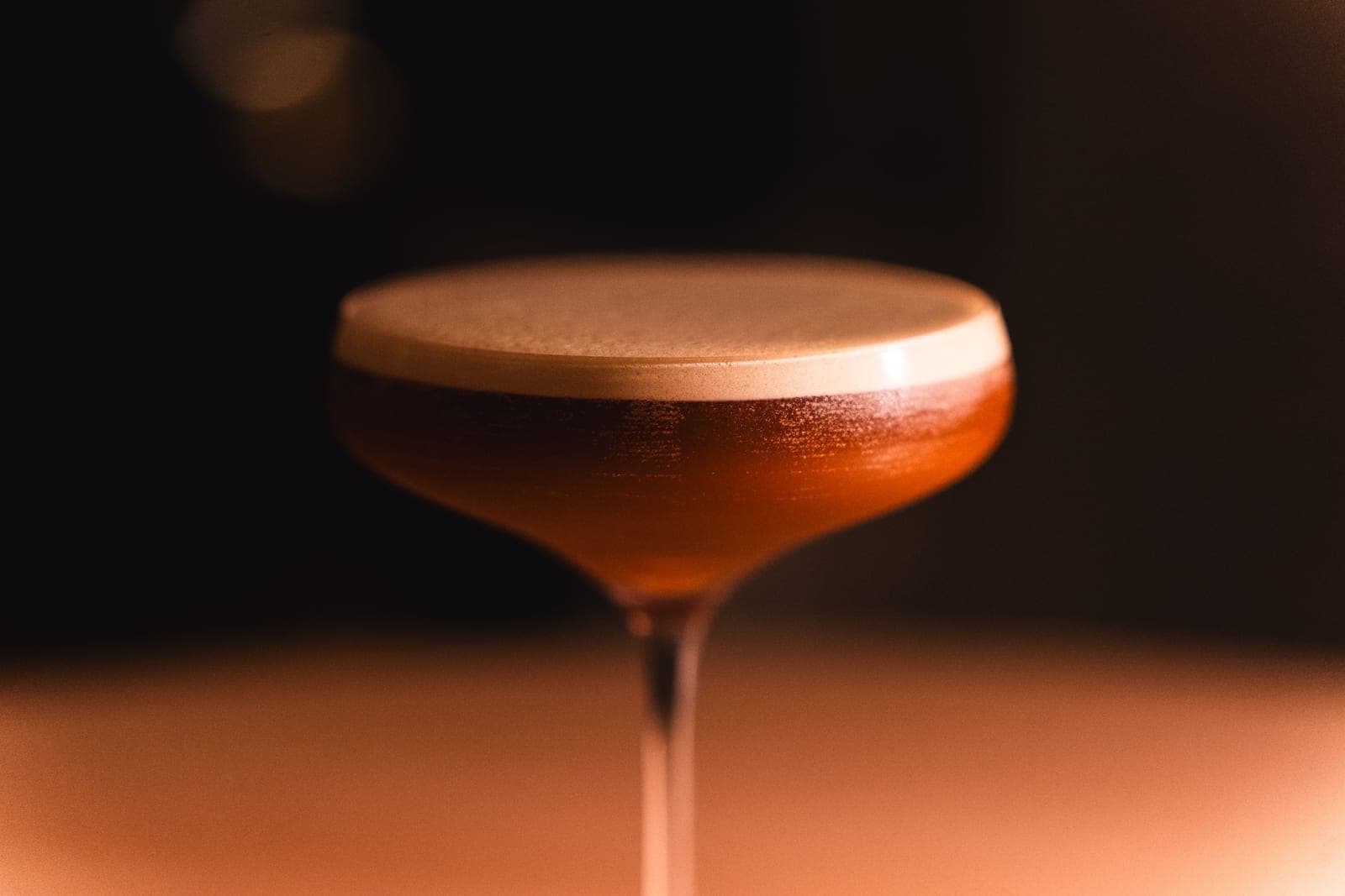 A coupe and a rocks glass side by side on a warm-lit bar top