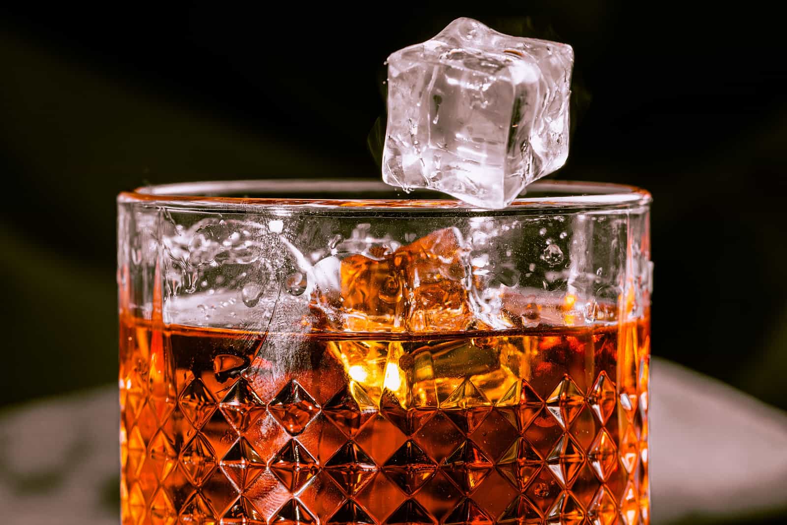 A large clear ice cube in a rocks glass under warm bar light