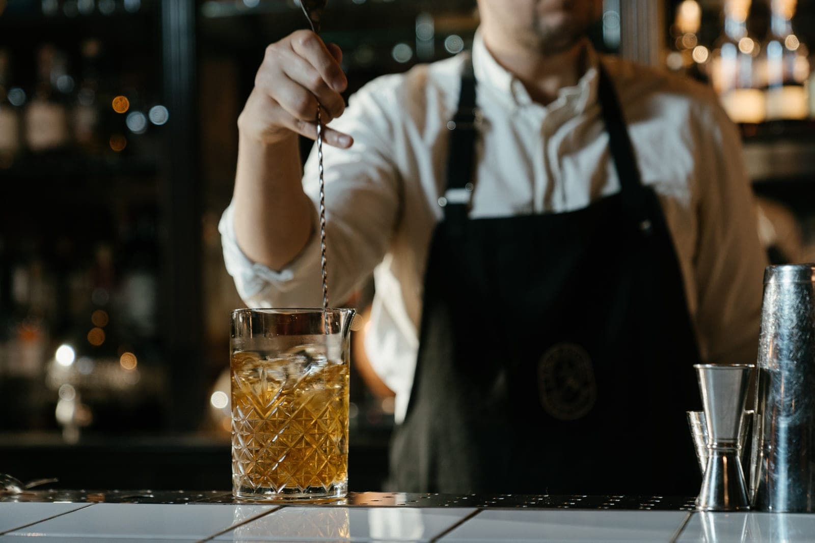 A jigger, bar spoon and cut-glass mixing glass on a wooden bar