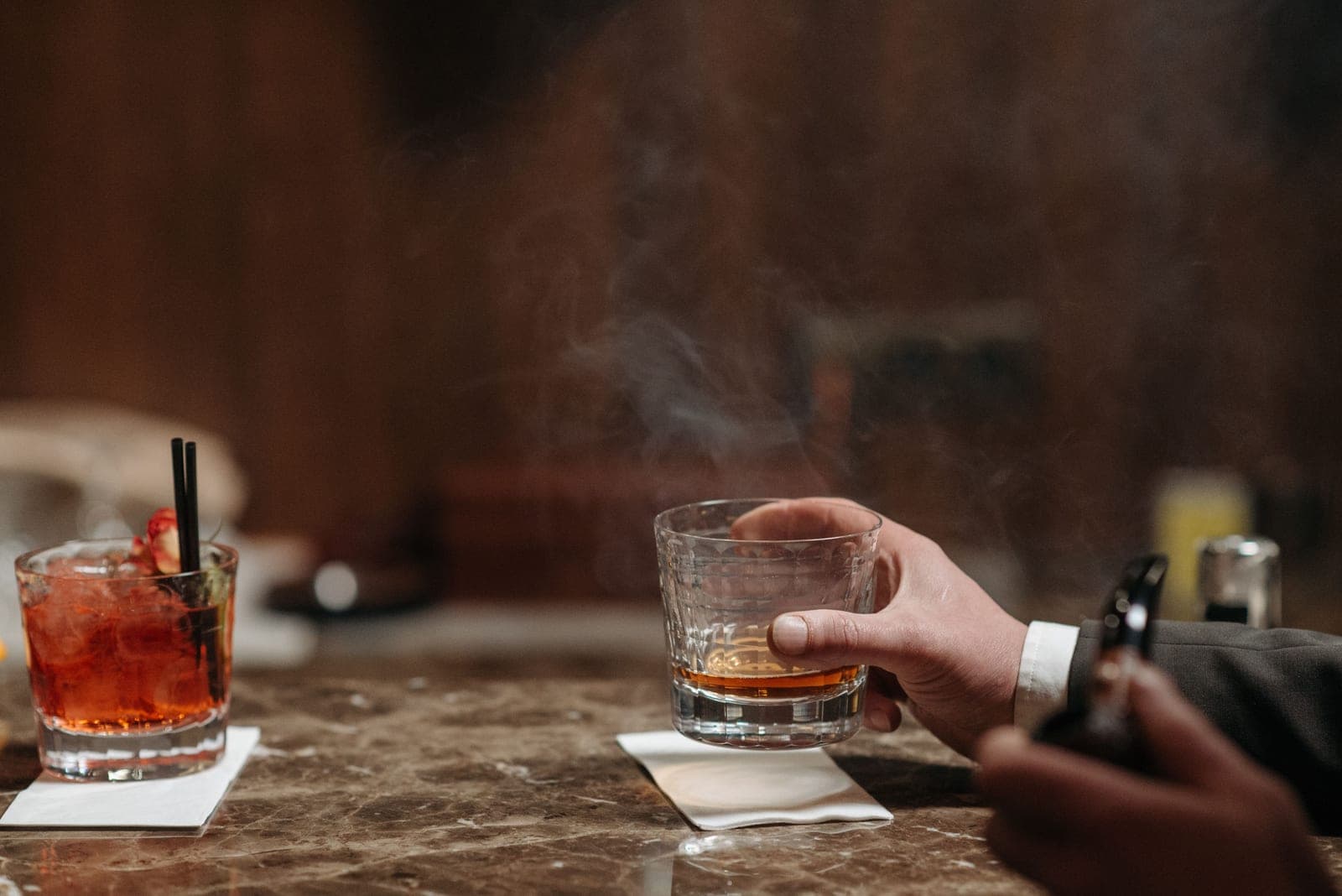 Smoke settling over a rocks glass on a dark wooden bar