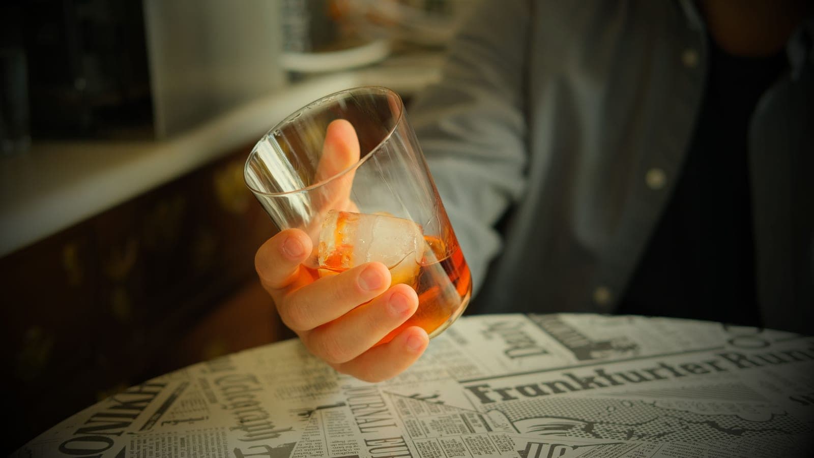 A heavy rocks glass holding whiskey over a large clear cube